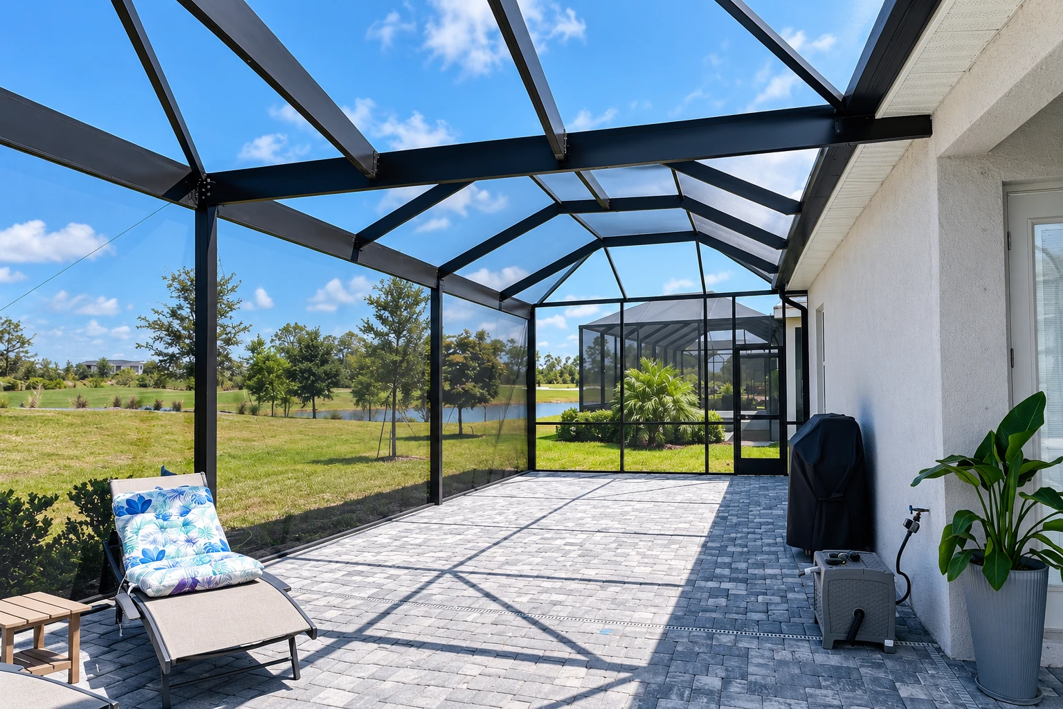 Enclosed patio room with a black-framed screen enclosure, paved floor, and a sunny lawn beyond.