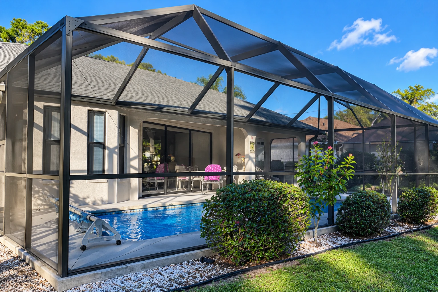 Screened patio enclosure with a dark metal frame surrounding a backyard swimming pool.