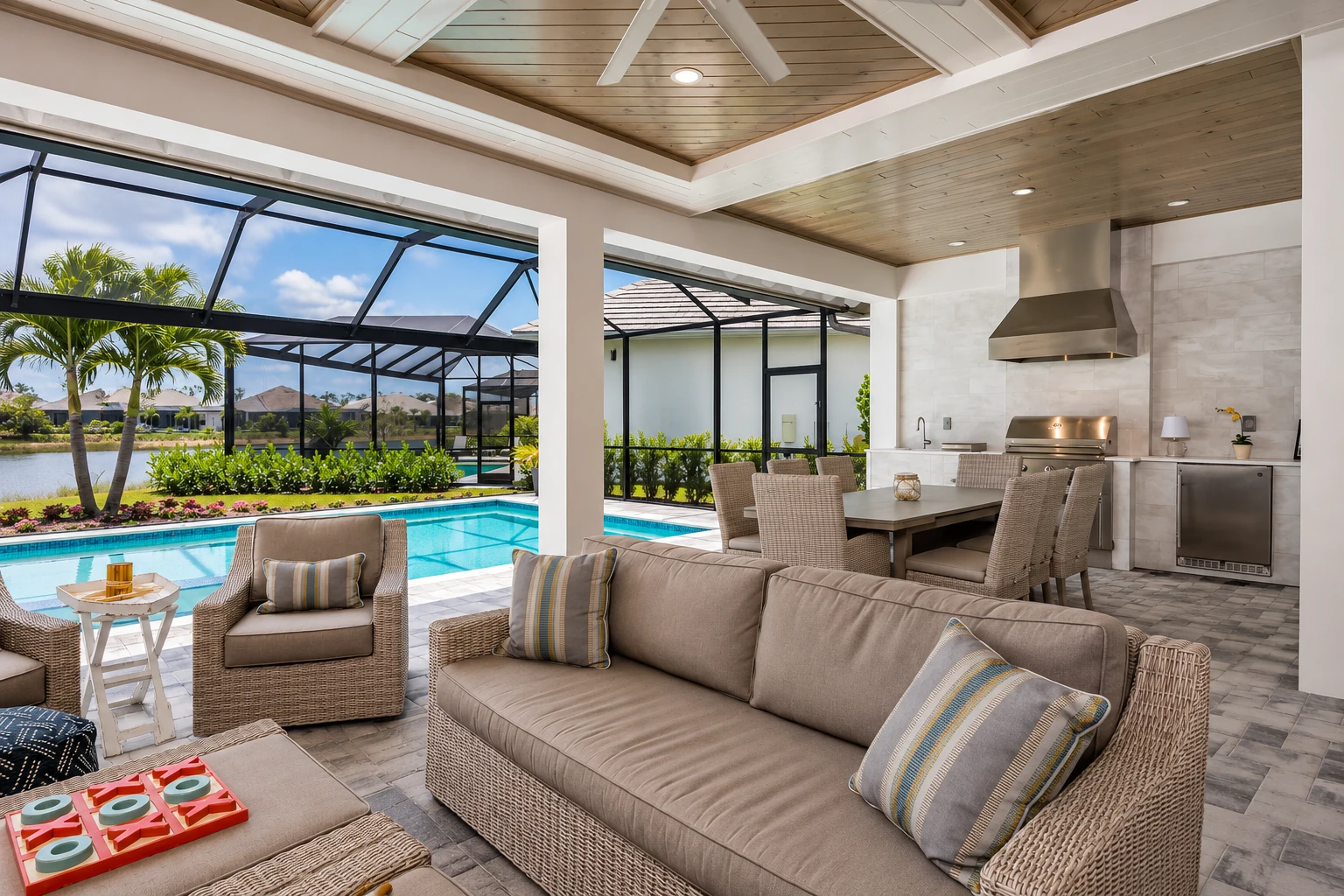 Screened-in patio room with wicker seating, a dining table, and an outdoor kitchen beside a swimming pool.