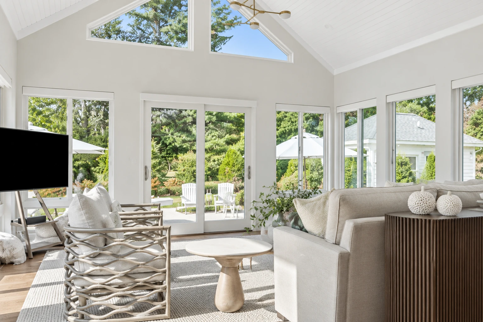 Bright white sunroom with vaulted ceilings, large windows, and neutral seating overlooking a garden.